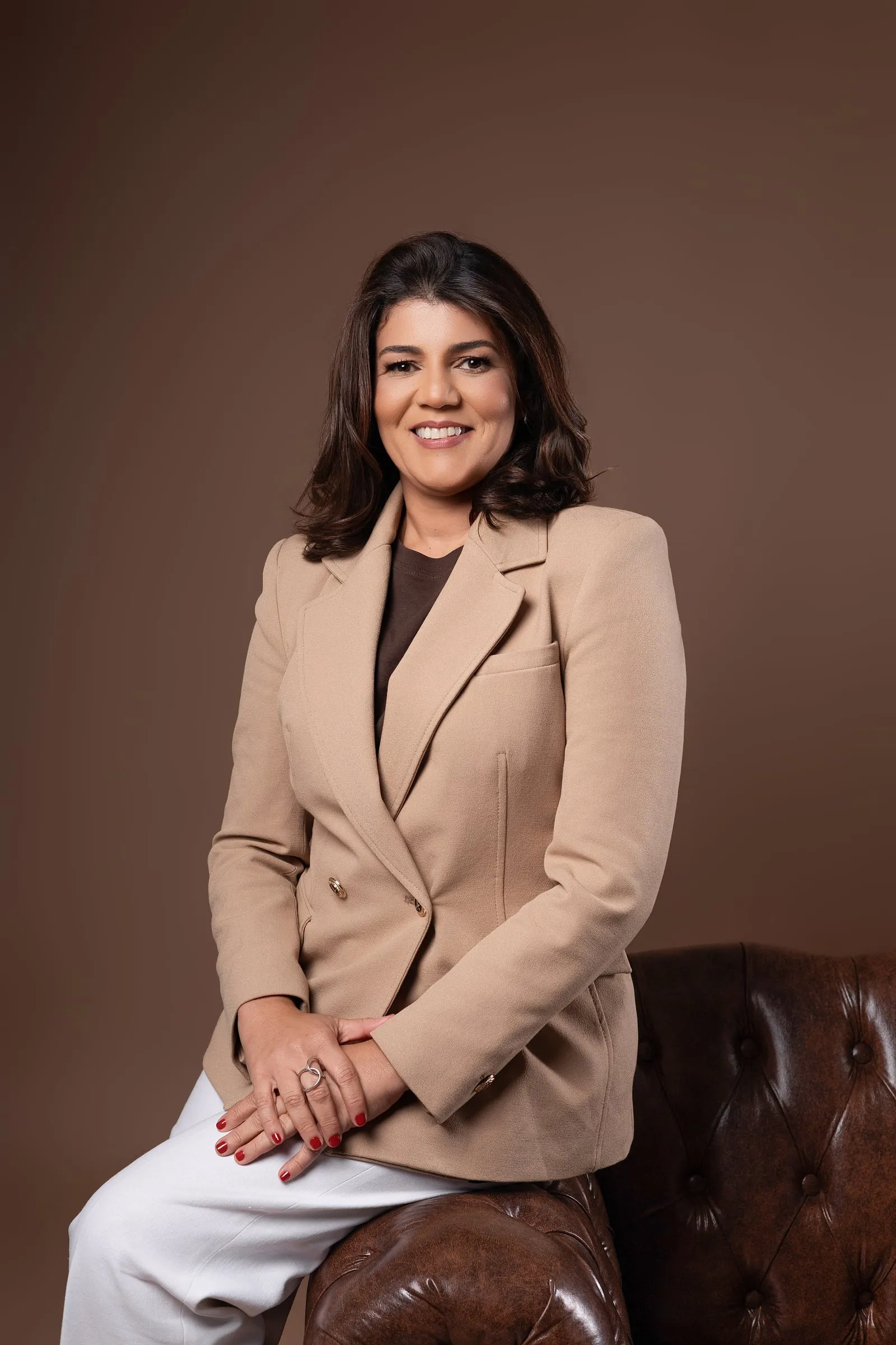 Dra. Lilian Figueiredo, de blazer bege, sentada no braço de um sofá de couro